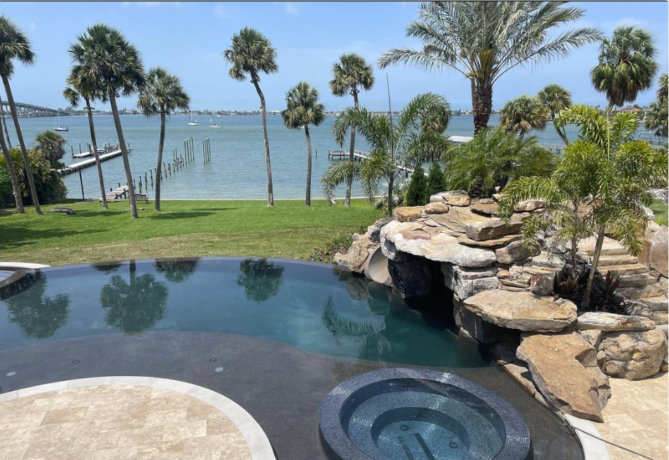 A beautiful swimming pool overlooks a bright blue ocean and palm trees.