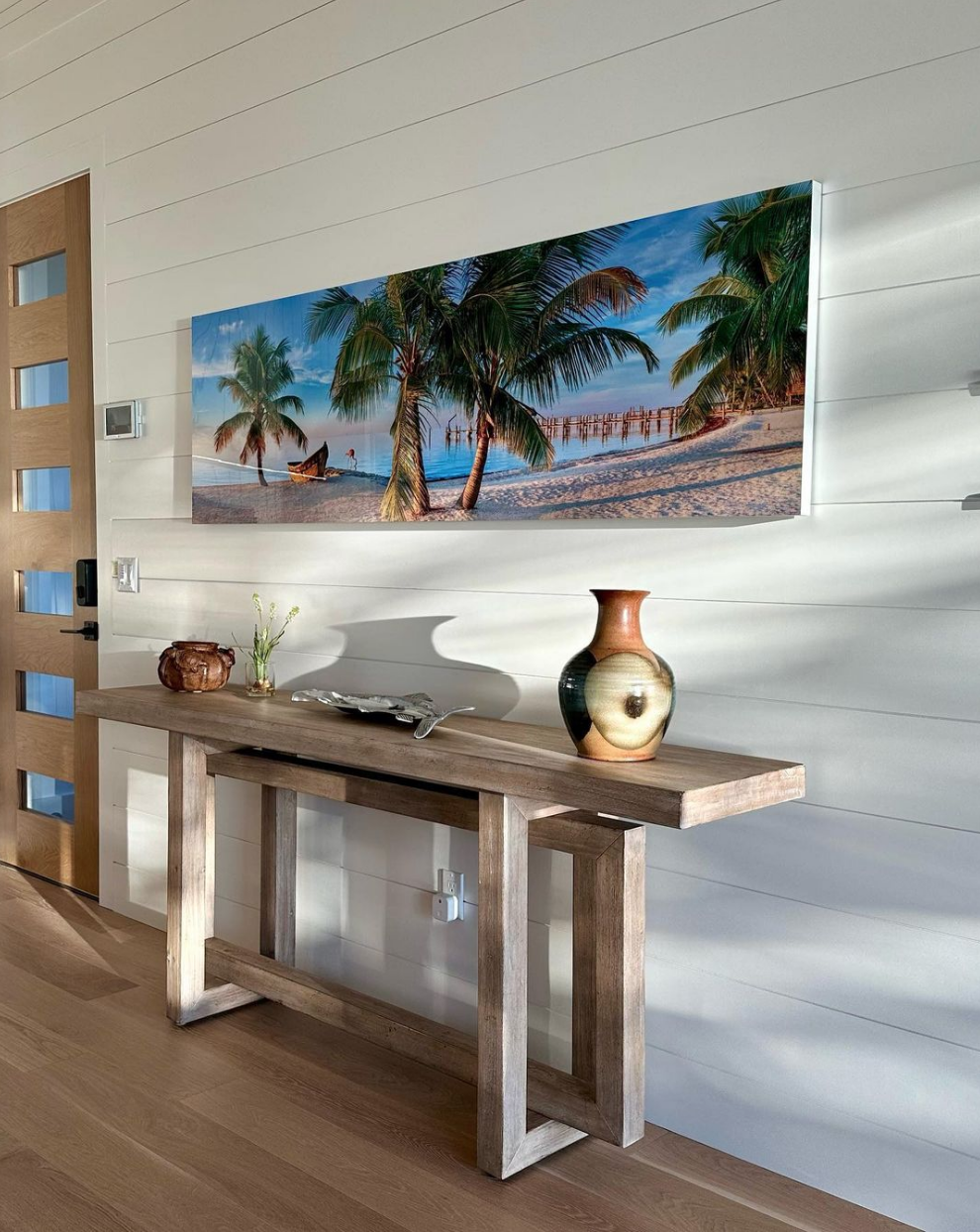 A beautiful wooden table sits under a beach painting in a home entryway
